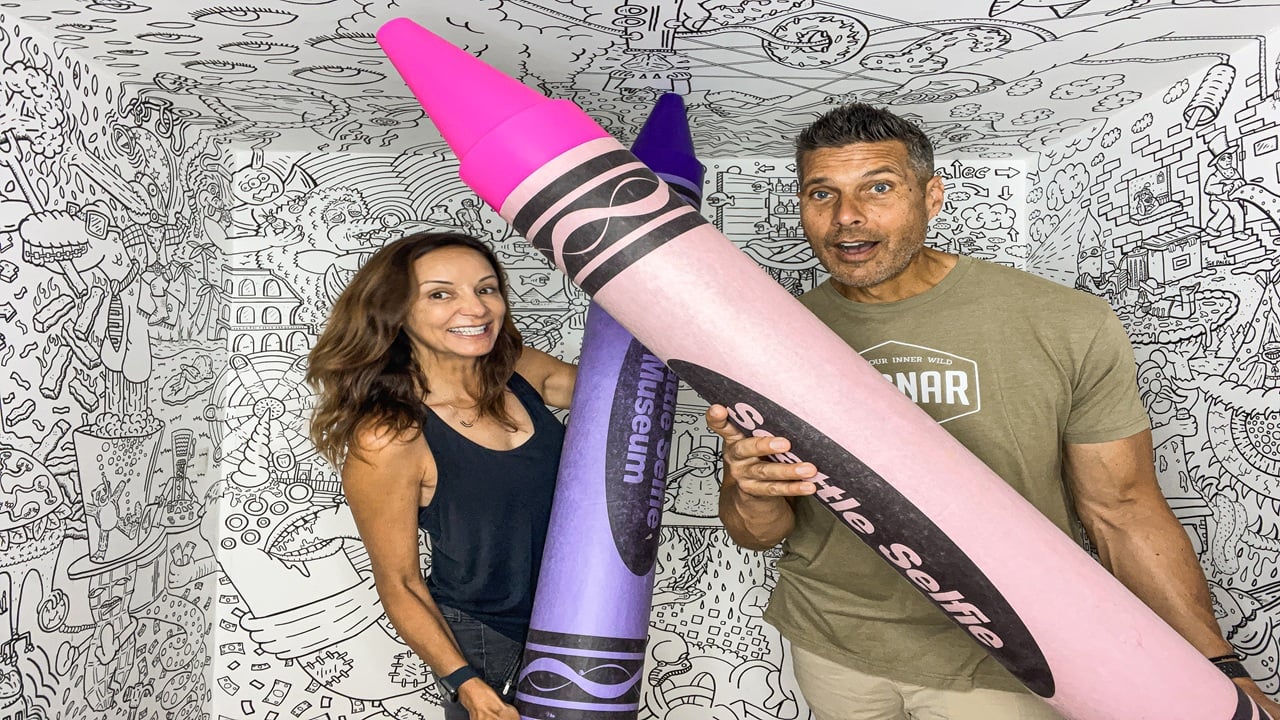 Couple holding giant crayons in a room with coloring books for walls